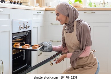 Young Islamic Housewife In Hijab And Apron Baking Muffins In Kitchen, Taking Tray With Hot Cupcakes Out Of Oven, Millennial Muslim Woman In Headscarf Enjoying Cooking At Home, Closeup Shot