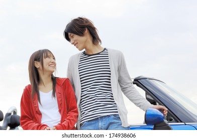 Young Japanese Couple Talking While Leaning On Car