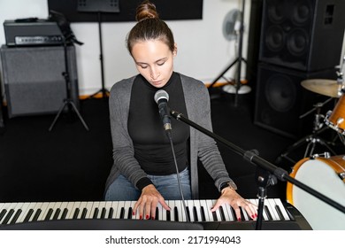 Young Japanese Or European Brunette Woman Singing Lyrical Song On Mic And Playing Digital Keyboard Electronic Piano Alone Near Drums In Music Studio. Learning And Practicing Before Exam In School