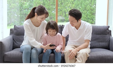 Young Japanese Family Using Smart Phone Sitting On The Sofa