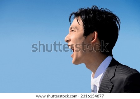 A young Japanese male office worker in his 20s shouting to the sky on the rooftop. Close-up on his face.