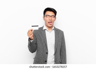 Young Japanese Man With Cheerful, Carefree, Rebellious Attitude, Joking And Sticking Tongue Out, Having Fun. Credit Card Concept.