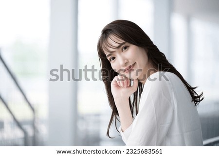 A young Japanese woman in casual clothing, smiling and looking at the camera. An image of office casual working in an office, changing jobs or finding employment.