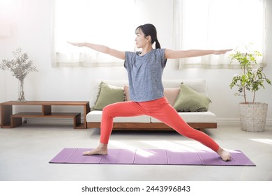 A young Japanese woman doing Warrior Poses in the living room, stretching, exercising, working out or yoga. - Powered by Shutterstock