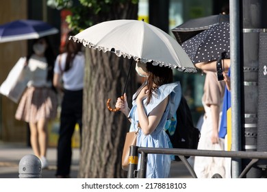 Young Japanese woman protecting herself from the sun with an umbrella in Tokyo on a hot summer day. - Shutterstock ID 2178818103