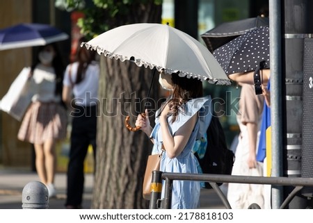 Young Japanese woman protecting herself from the sun with an umbrella in Tokyo on a hot summer day.