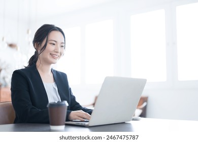 A young Japanese woman in a suit operating a computer and other devices in a beautifully backlit office. Close-up of upper body. Copy space available. - Powered by Shutterstock