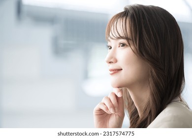 A young Japanese woman in a suit staring into the distance with a smile. An image of suits working in an office, changing jobs or finding employment.