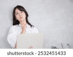 Young Japanese woman thinking upwards with a computer. Grey back. Thinking about changing jobs and retirement.