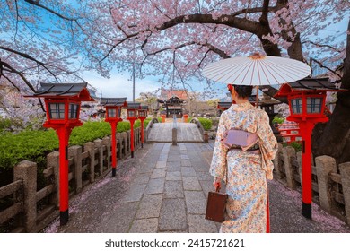 Young Japanese woman in a  traditional Kimono dress strolls by Rokusonno shrine during full bloom sakura cherry blossom period in Kyoto, Japan