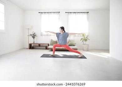 
Young Japanese woman in warrior pose in living room, stretching, exercising, working out, yoga. Wide angle view of the room. - Powered by Shutterstock