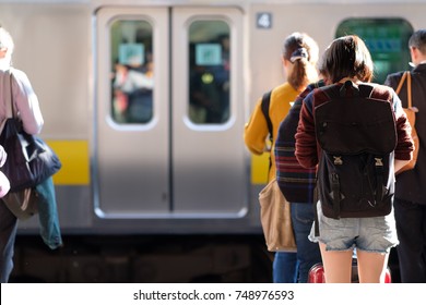Young Japanese woman wearing shorts and carrying a black backpack hunched over her phone while while waiting for her train in a railway station in Tokyo.