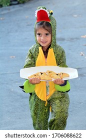 Young Jewish Girl (age 5) Wearing Alligator Costume Carry Mishloach Manot (Purim Basket) With Oznei Haman (Jewish Triangular Filled-pocket Cookie) For Purim Jewish Holiday.