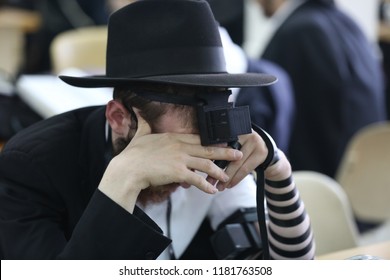 A young Jewish man covered in leather straps known in Judaism as "Tefillin," prays in deep concentration while covering his eyes, in a synagogue