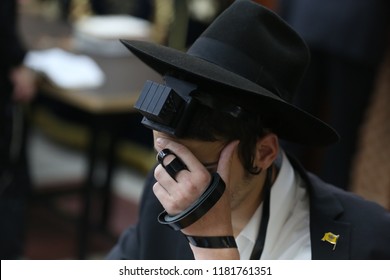 A young Jewish man recites the "shema yisrael" prayer (translates to: hear o' Israel prayer) while donning leather straps, a black hat, and covering his eyes with hand