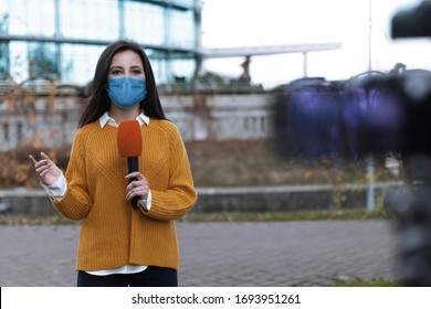 Young journalist with medical mask and microphone working on city street. Virus protection - Shutterstock ID 1693951261