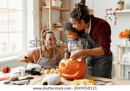 Young joyful african american family mother, father and boy son enjoying Halloween preparation at home, parents and kid making jack o lantern and painting pumpkins for Saints Day celebration