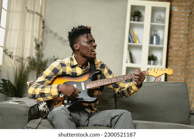 Young joyful african american man playing guitar in living room. Happy man enjoy at home. - Powered by Shutterstock