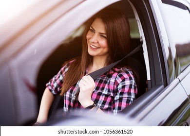 Young joyful beautiful girl is buckling up in a drivers seat of her car.
