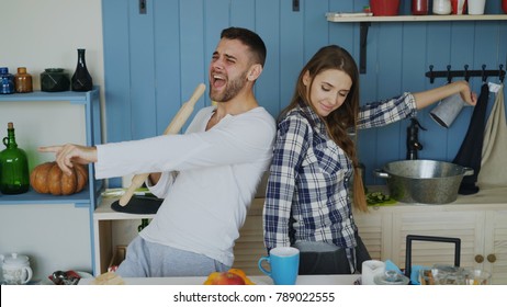 Young Joyful Couple Have Fun Dancing And Singing While Set The Table For Breakfast In The Kitchen At Home