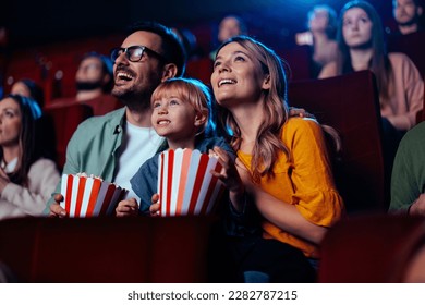 A young joyful couple is with their daughter in the cinema, watching an exciting movie.
