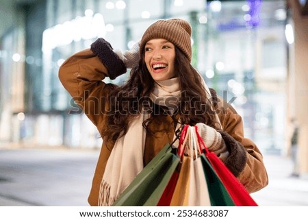 Young joyful European woman with colorful shopper bags enjoy seasonal winter sales, posing on the background of shopping mall outdoors