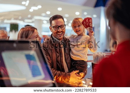A young joyful family is buying movie tickets at the cash register in the theater.