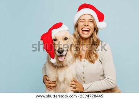 Young joyful owner woman wears casual clothes Santa hat hug cuddle embrace best friend pet retriever dog wink isolated on plain pastel blue background studio. New Year Christmas celebration concept