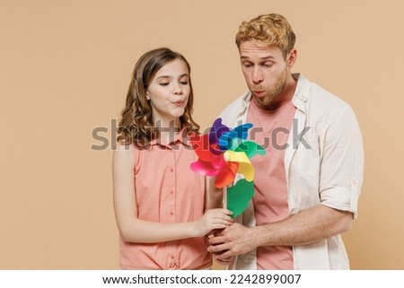Young joyful parent man have fun with child teen girl in casual clothes Daddy little kid daughter blowing on toy windmill isolated on beige background studio portrait. Father's Day Love family concept