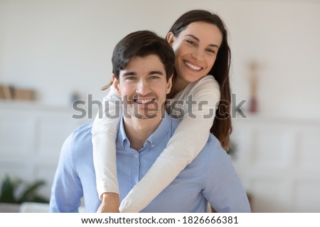 Young and joyful. Portrait of happy laughing playful millennial spouses cuddling, having fun and looking at camera, elder brother student piggybacking teenage younger sister posing for cute picture