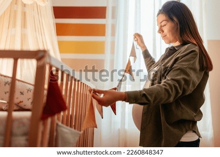 A young joyful pregnant woman is at home decorating the baby nursery.