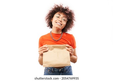 Young Joyful Woman With Afro Curls In Orange Clothes Holding Craft Package Isolated On White Studio Background, Food Delivery, Eco Bag, Kazakh Caucasian Girl With Gift