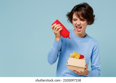 Young joyful woman in sweater looking camera hold a box with fastfood french fries potato burger add sauce isolated on plain pastel light blue background studio portrait. People lifestyle food concept - Powered by Shutterstock