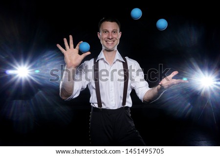 young juggler guy poses for the camera and juggles with blue balls in a circus