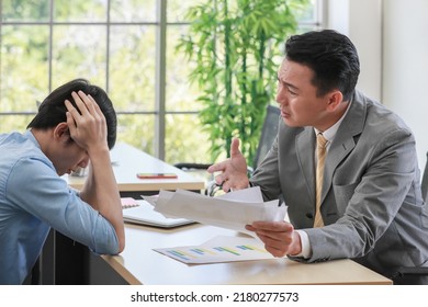 A Young Junior Employee Holding His Head With Stress And Upset While Senior Boss Businessman Abuses Him About Low Quality And Wrong Work. Daily Working Problem In Office Concept.