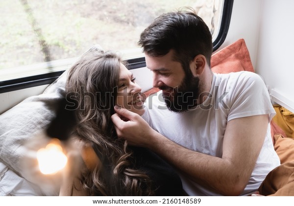 Young just married couple is traveling in\
travel van. Romantic atmosphere of relaxation. Road trip around\
country for weekend. Caucasian man and woman lying in bedroom in\
camper. Millennial\
generation