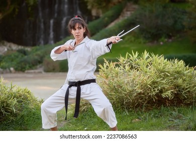 Young karate woman in fighting stance holding a pair of sai outdoors. High quality photo - Powered by Shutterstock