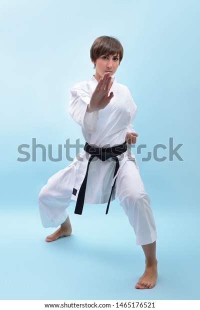 Young karate woman in a white kimono with black belt\
demonstrates fighting stances and strikes. Girl at studio shows\
martial arts