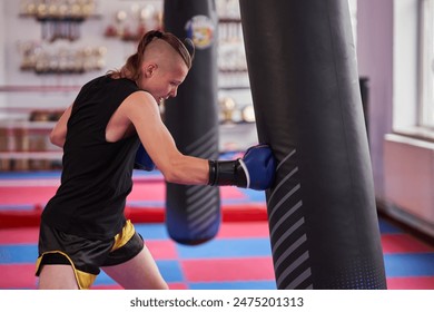 Young kickboxer training on the heavy bag in the gym, the ring is in background - Powered by Shutterstock