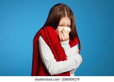 Young kid feels unwell, blows nose in white tissue, suffers from running nose, cold symptoms or allergy, sneezes very often, wearing red scarf
