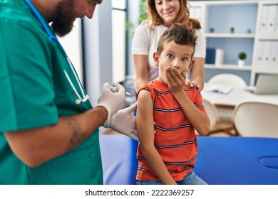 Young Kid Getting Vaccine At Doctor Clinic Covering Mouth With Hand, Shocked And Afraid For Mistake. Surprised Expression 