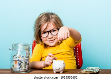 Young Kid Girl Putting Money Into A Piggy Bank. Child And Money. How To Save. Financial Education For Children.