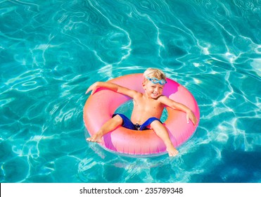 Young Kid Having Fun In The Swimming Pool On Inner Tube Raft. Summer Vacation Fun. 