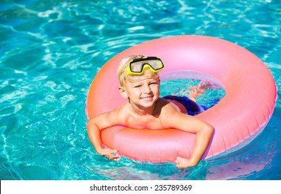 Young Kid Having Fun In The Swimming Pool On Inner Tube Raft. Summer Vacation Fun. 