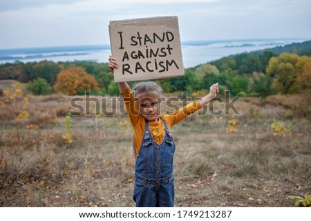 Young kid holding a poster with anti-racism message over beautiful nature background, activism and human rights movement, outdoor lifestyle