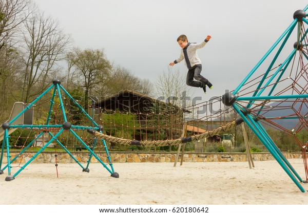 Young kid jumping from geometric\
dome structure at empty playground in Bilbao. Boy flying in the air\
at park. Accident, risk, danger, brave child\
concepts