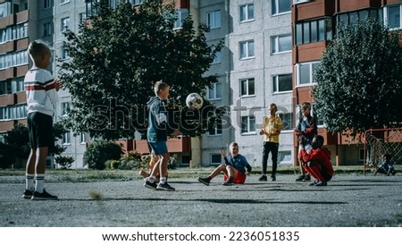 Young Kids Playing with Ball in the Neighborhood. Boy Practicing, Doing Kick-Ups. Teenager Dreaming of Becoming a Professional Football Player. Friends Cheering. Cold Desaturated Color Grading.