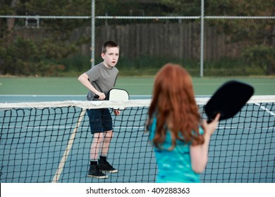 Young Kids Playing Pickleball On An Outdoor Court. 