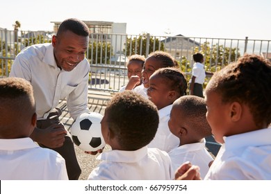 Young Kids In A School Playground With Teacher Holding Ball