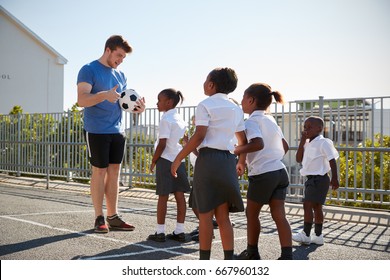 Young Kids In A School Playground With Teacher Holding Ball